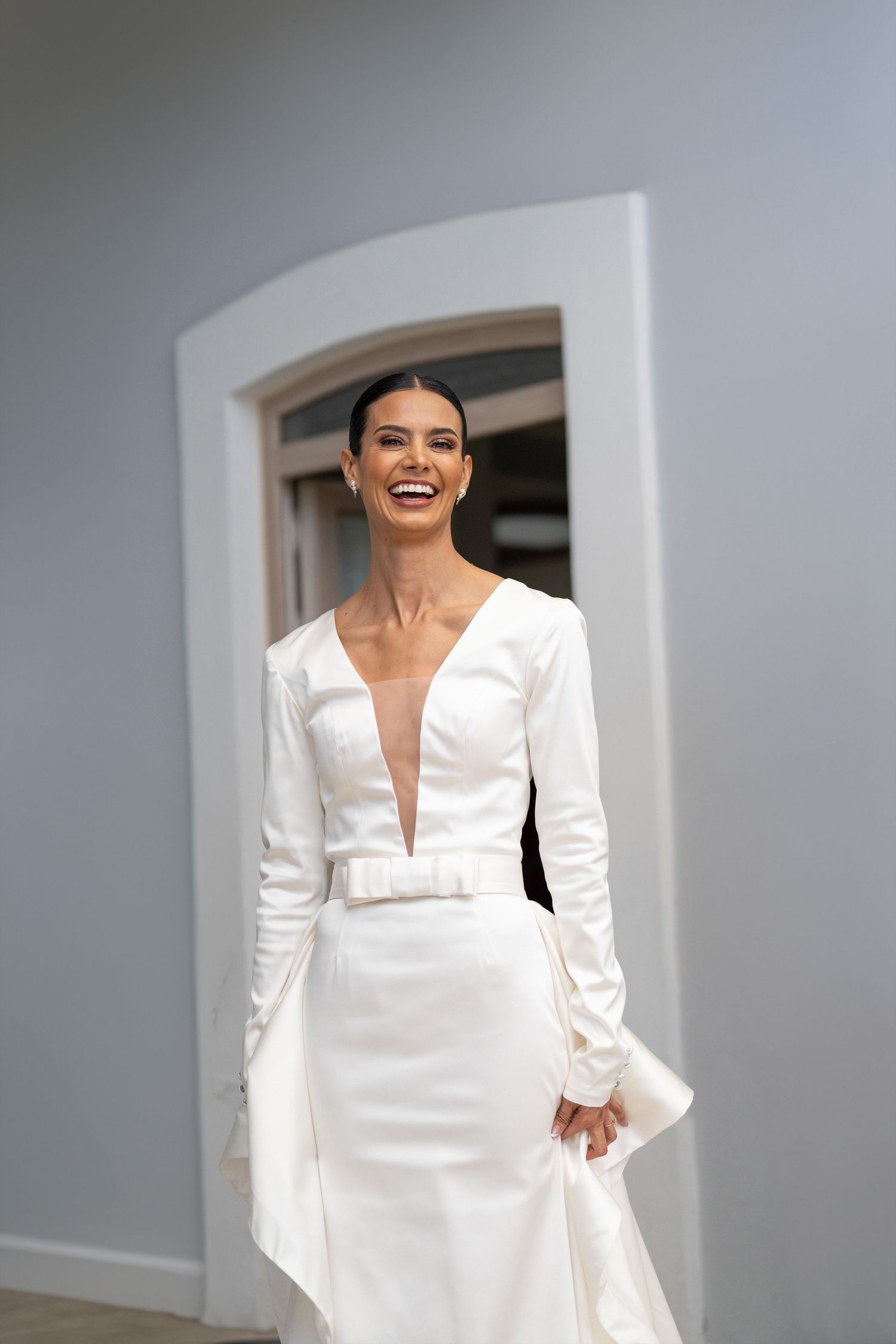 Radiant bride laughing in sleek white long-sleeve plunge neckline wedding gown.