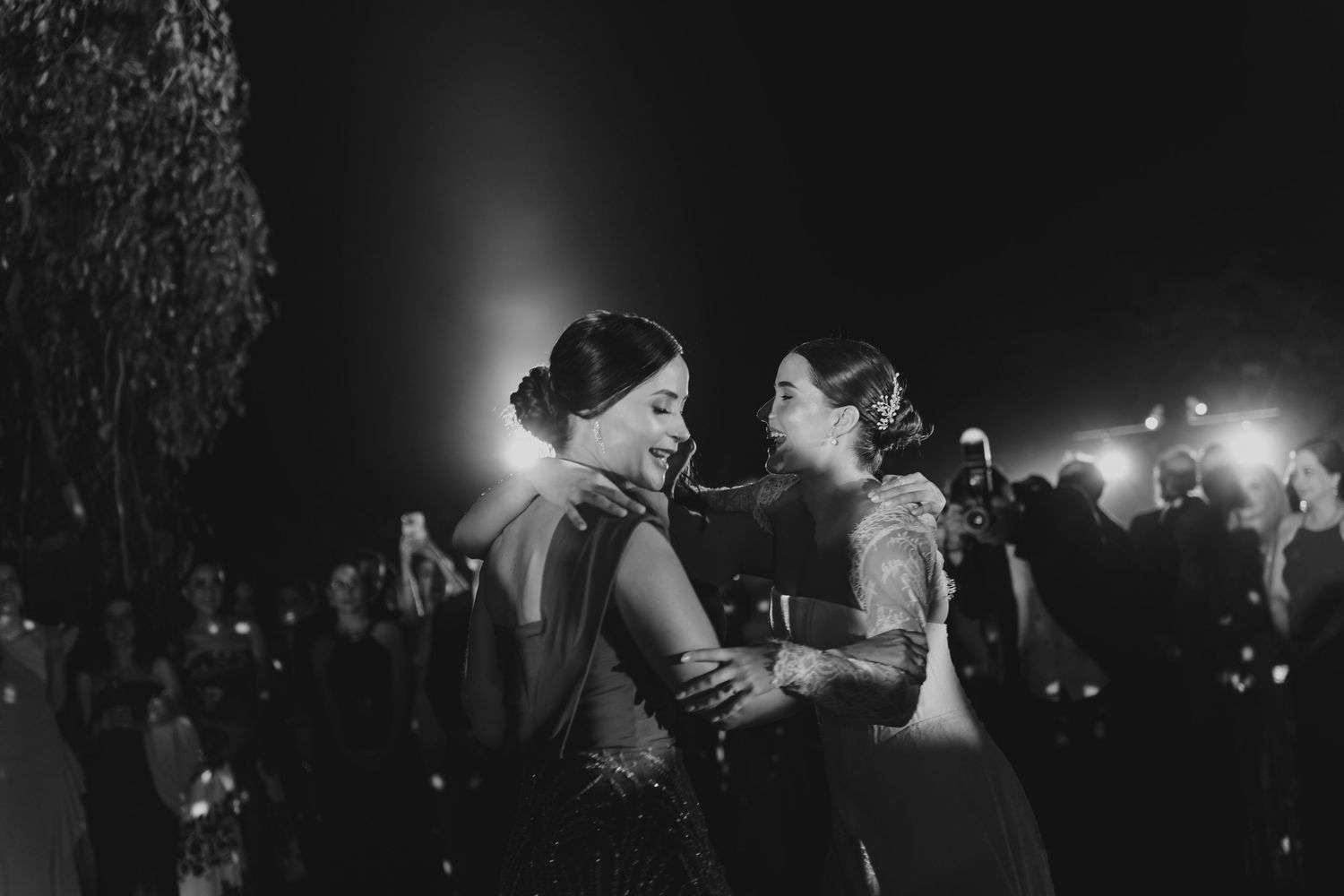 Black and white photo of bride sharing emotional embrace with guest at wedding reception.