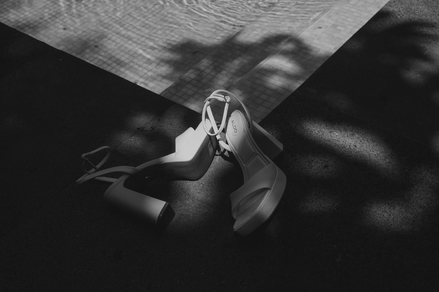Black and white artistic shot of bridal heeled sandals on floor with dramatic shadow patterns.