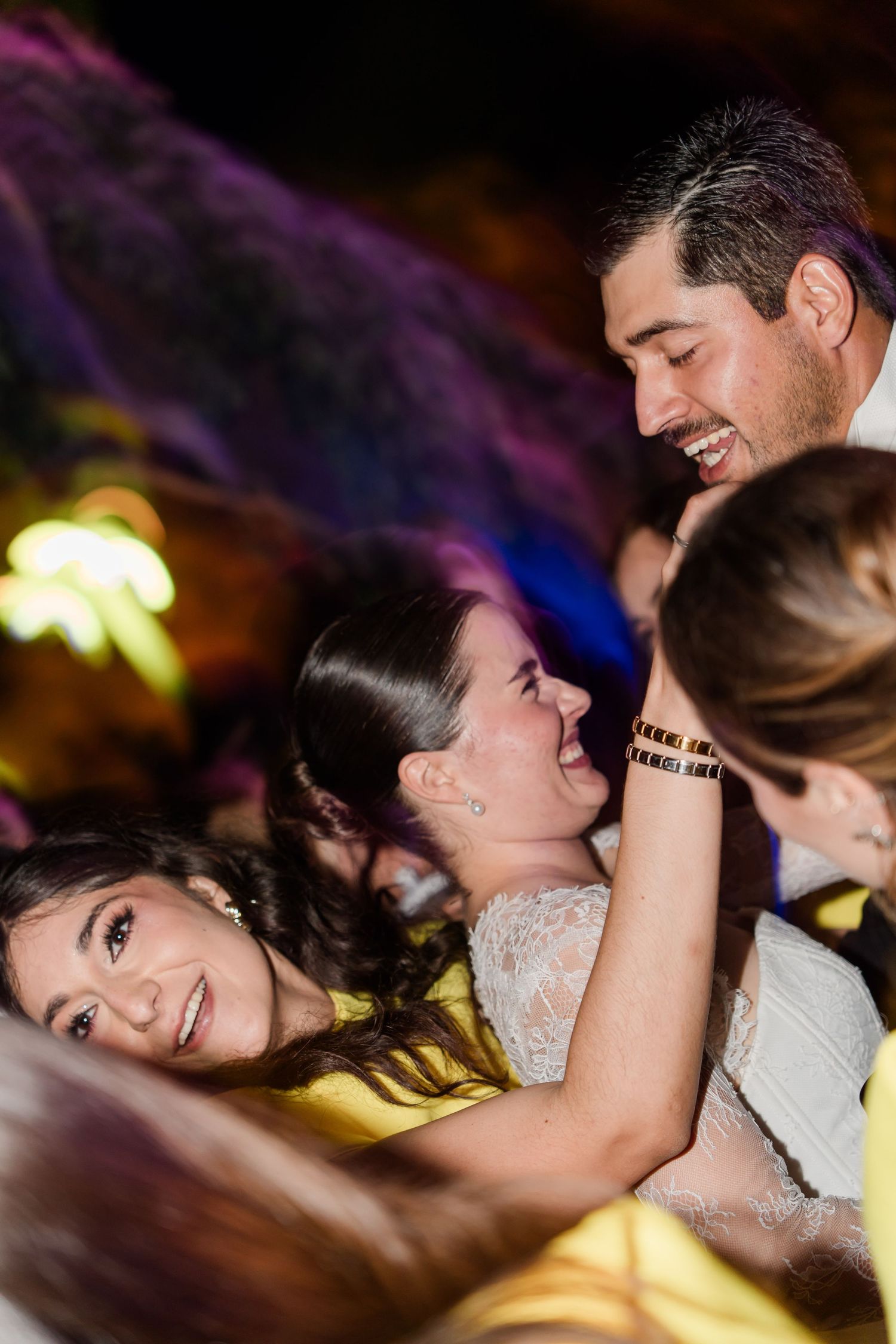 Bride and groom laugh joyfully with guests during an energetic wedding reception dance celebration.
