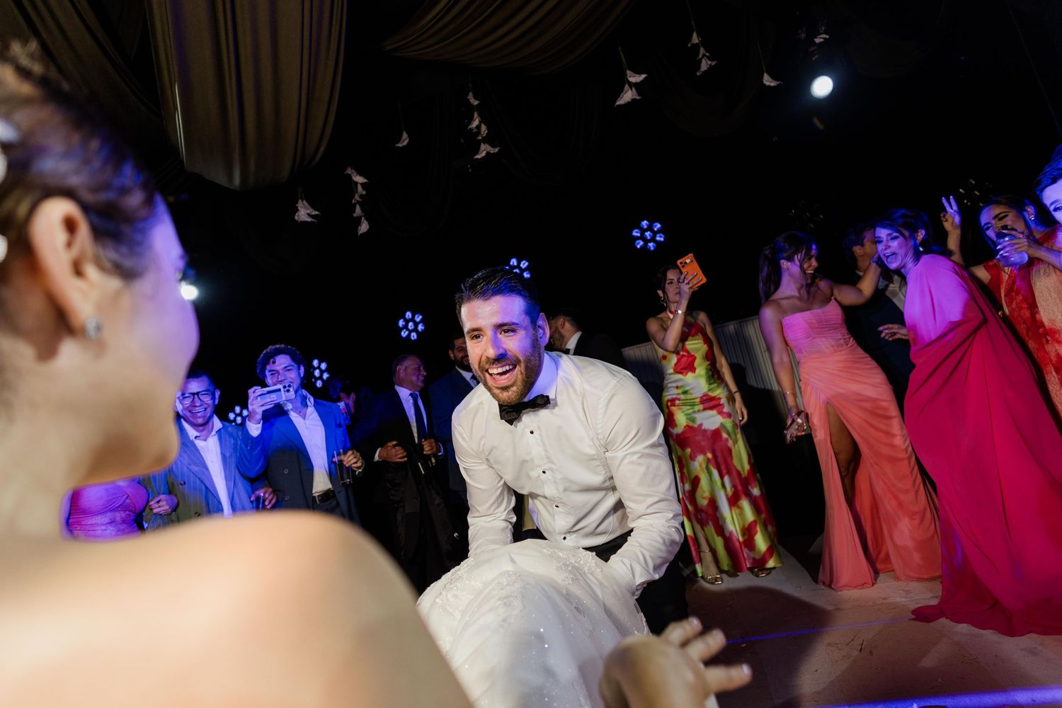 Joyful groom dancing energetically on the wedding reception dance floor surrounded by celebrating guests.