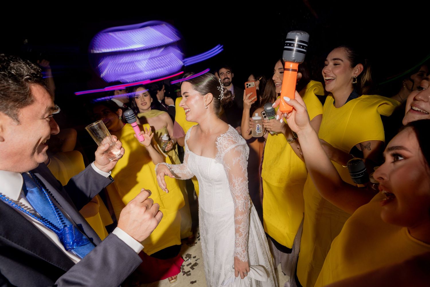 Bride celebrates with guests in yellow banana costumes during lively wedding reception toast.