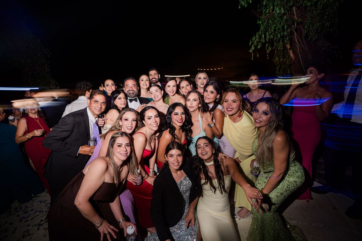 Large group of elegantly dressed wedding guests posing together for photo at night.