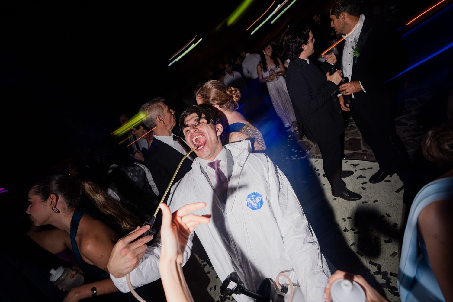 Man in white jumpsuit dancing energetically on a crowded wedding reception dance floor.