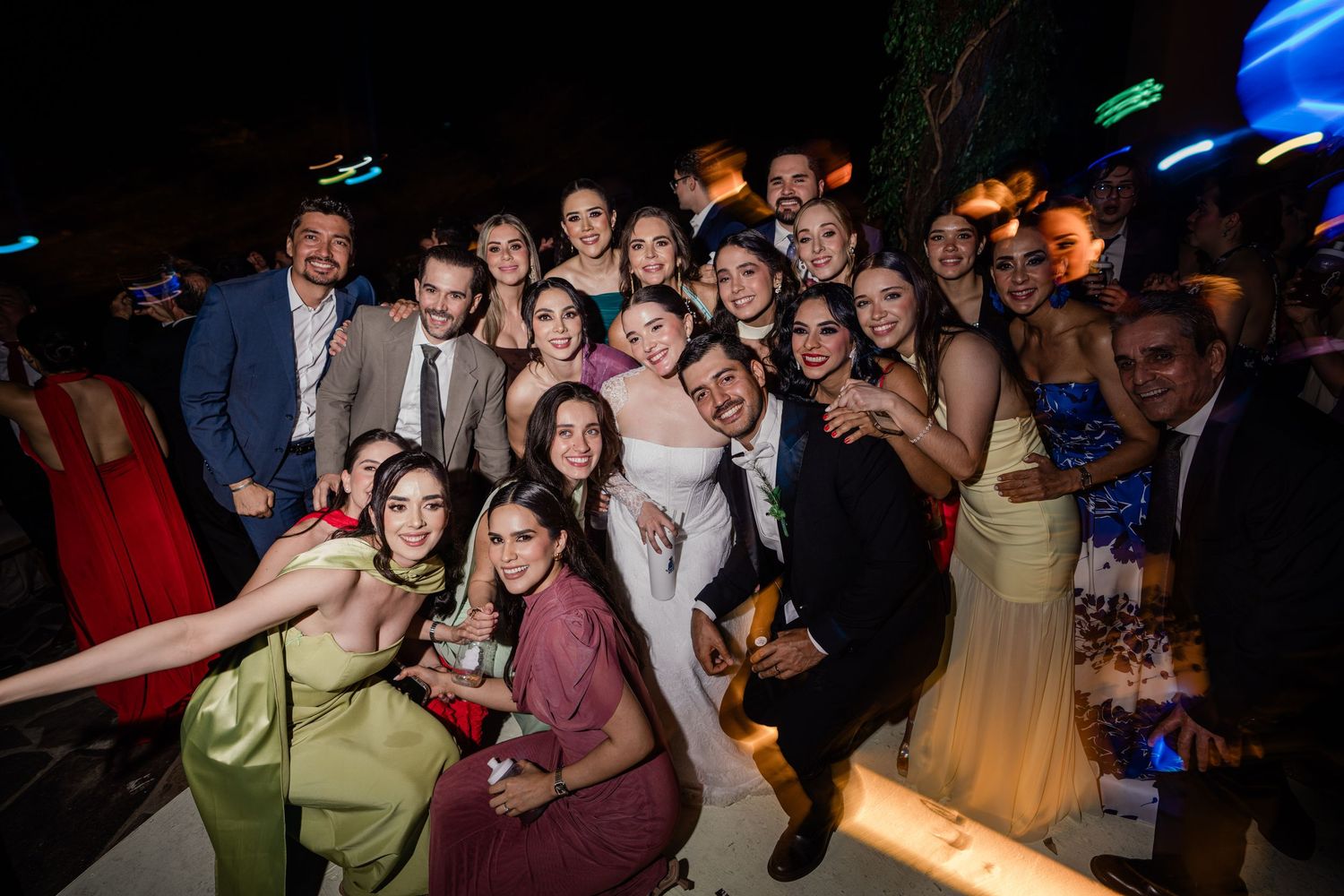 Large group of wedding guests pose for fun celebratory photo with bride and groom at reception.