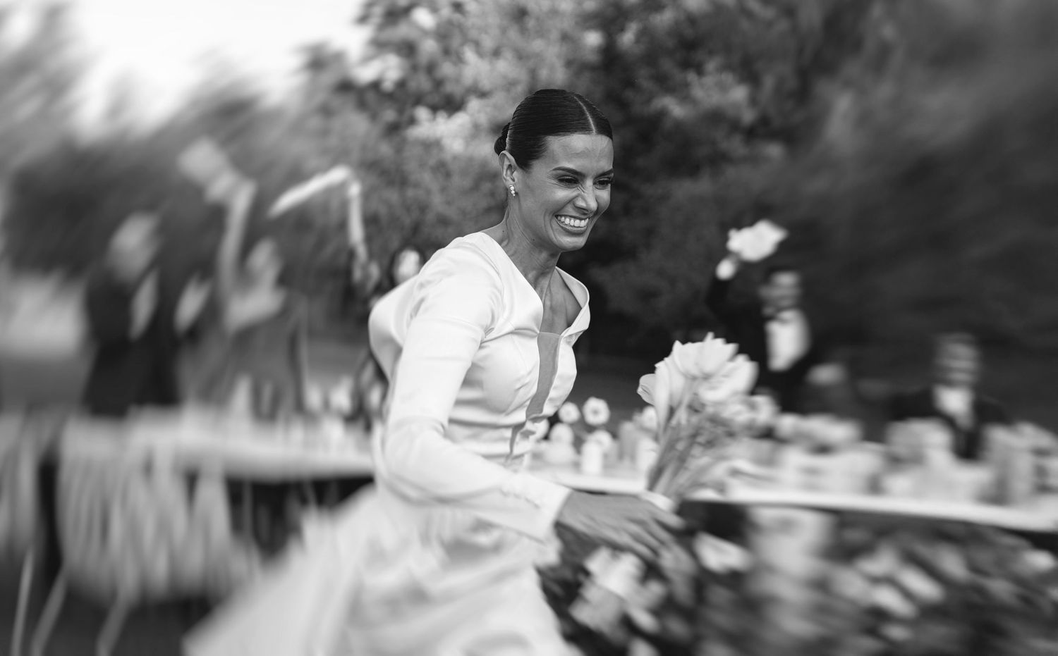 Black and white photo of smiling bride in white dress at outdoor wedding reception.