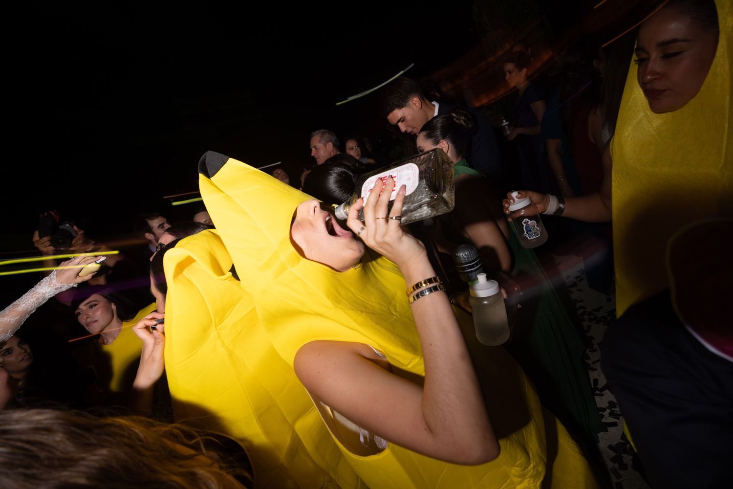 Wedding guest in yellow banana costume drinks at fun themed nighttime reception celebration.