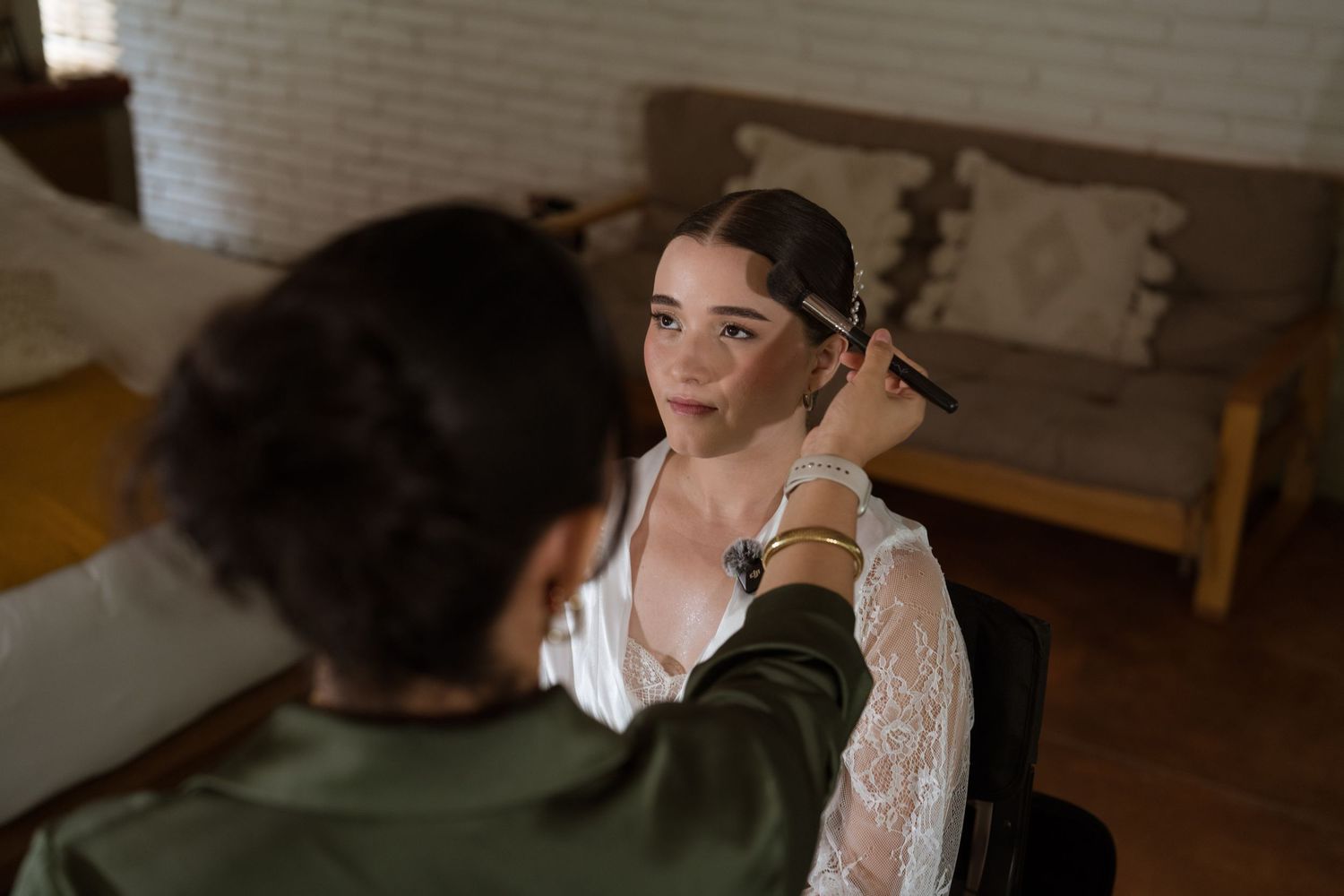 Makeup artist applying eyeshadow to bride in lace robe during wedding preparations.