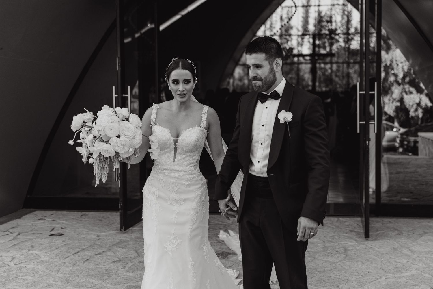 Bride and groom holding hands walking together in black and white wedding portrait outdoors.