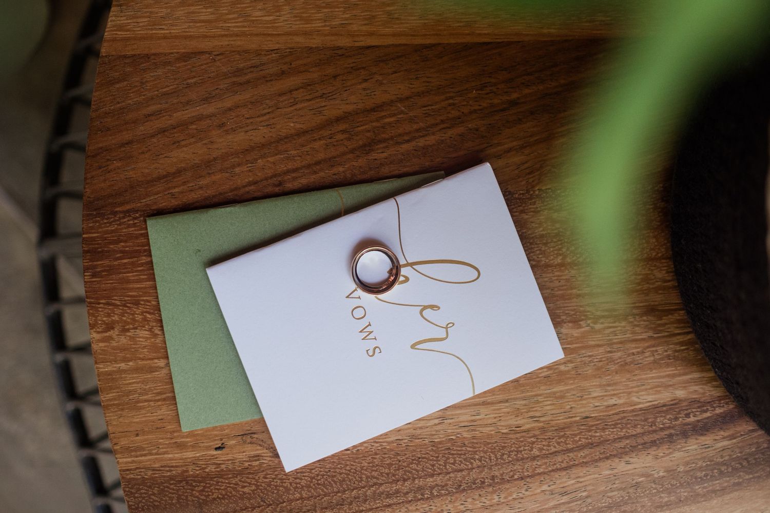 Gold wedding rings resting on white card with green envelope on wooden surface.