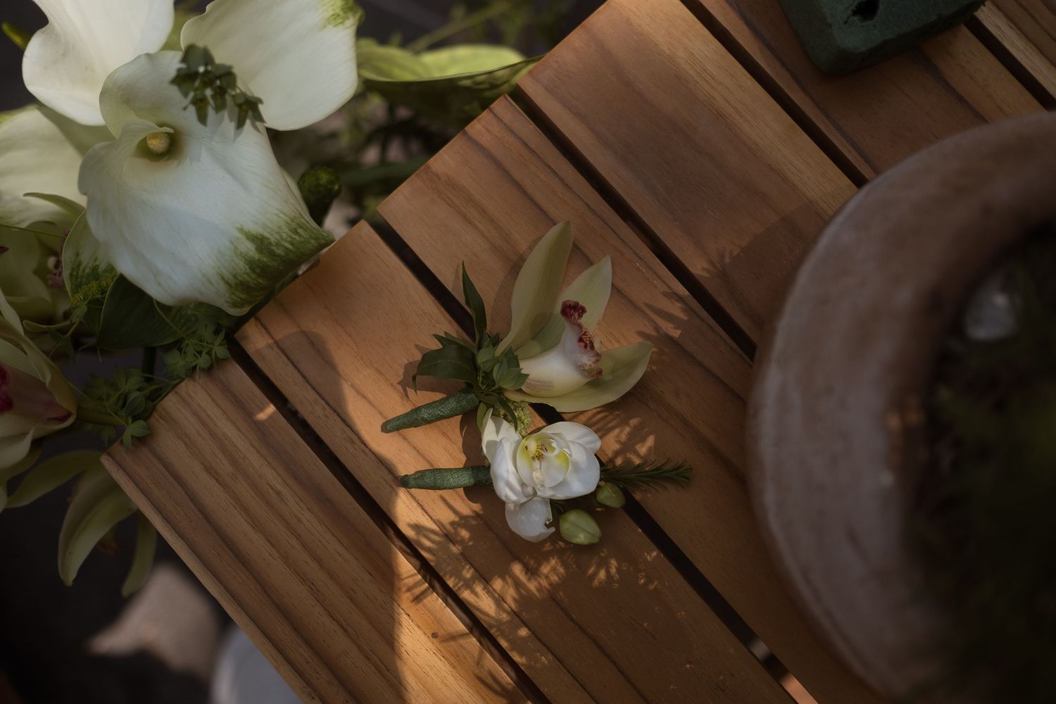 White floral boutonniere with green succulents resting on a wooden slatted table in natural light.