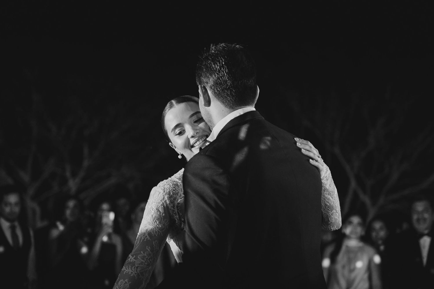 Black and white photo of a smiling bride dancing closely with groom at their elegant wedding reception.