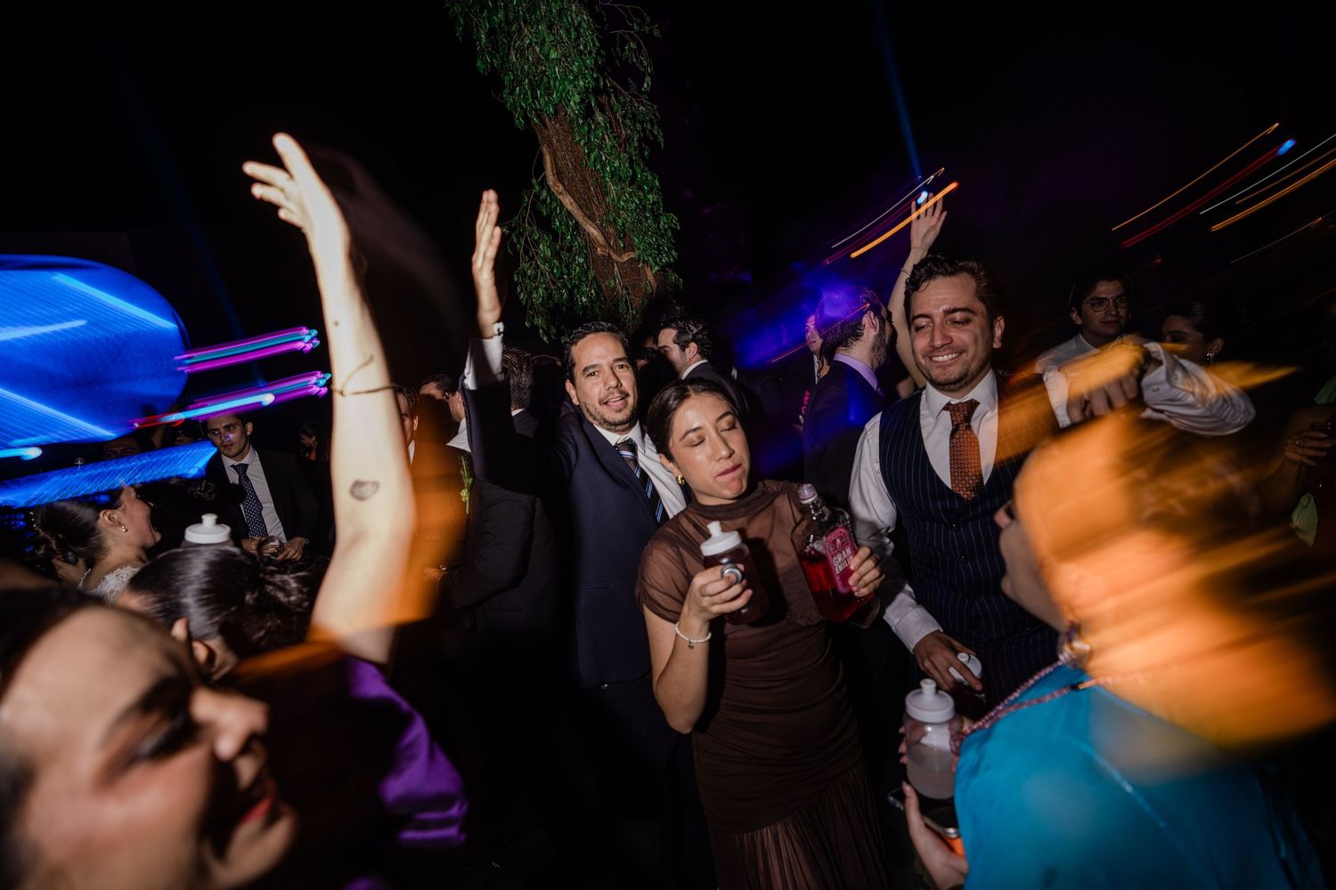 Wedding guests dance and celebrate energetically at vibrant nighttime outdoor reception party.