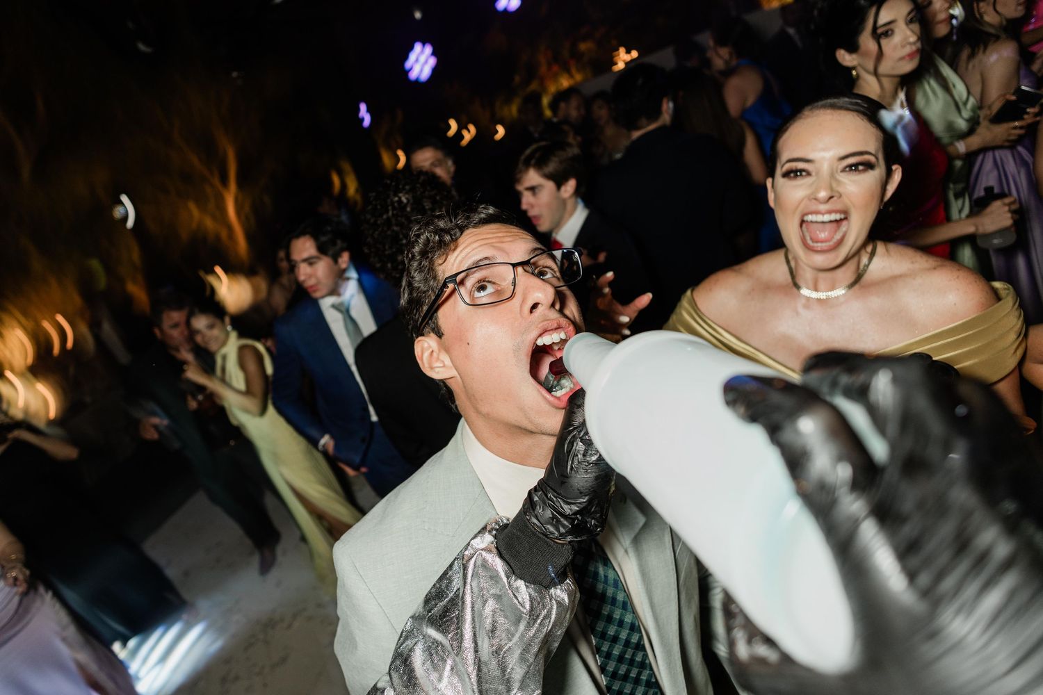Excited wedding guests dancing and laughing together at a lively indoor wedding reception party.