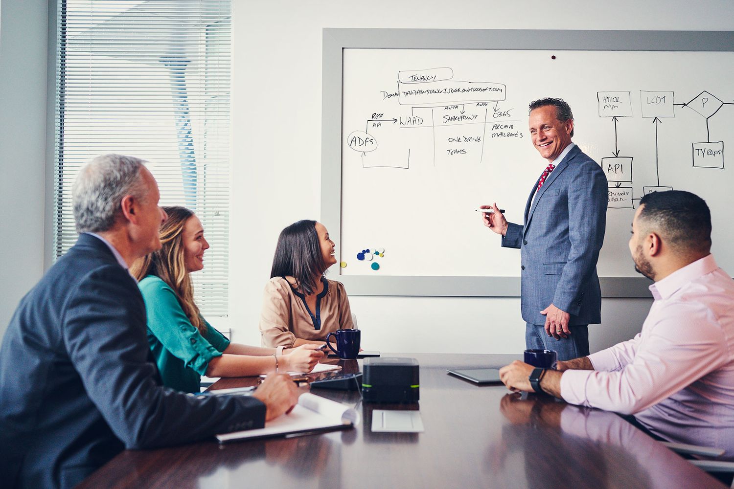 Business professional presents strategy on whiteboard to attentive colleagues in modern conference room meeting.