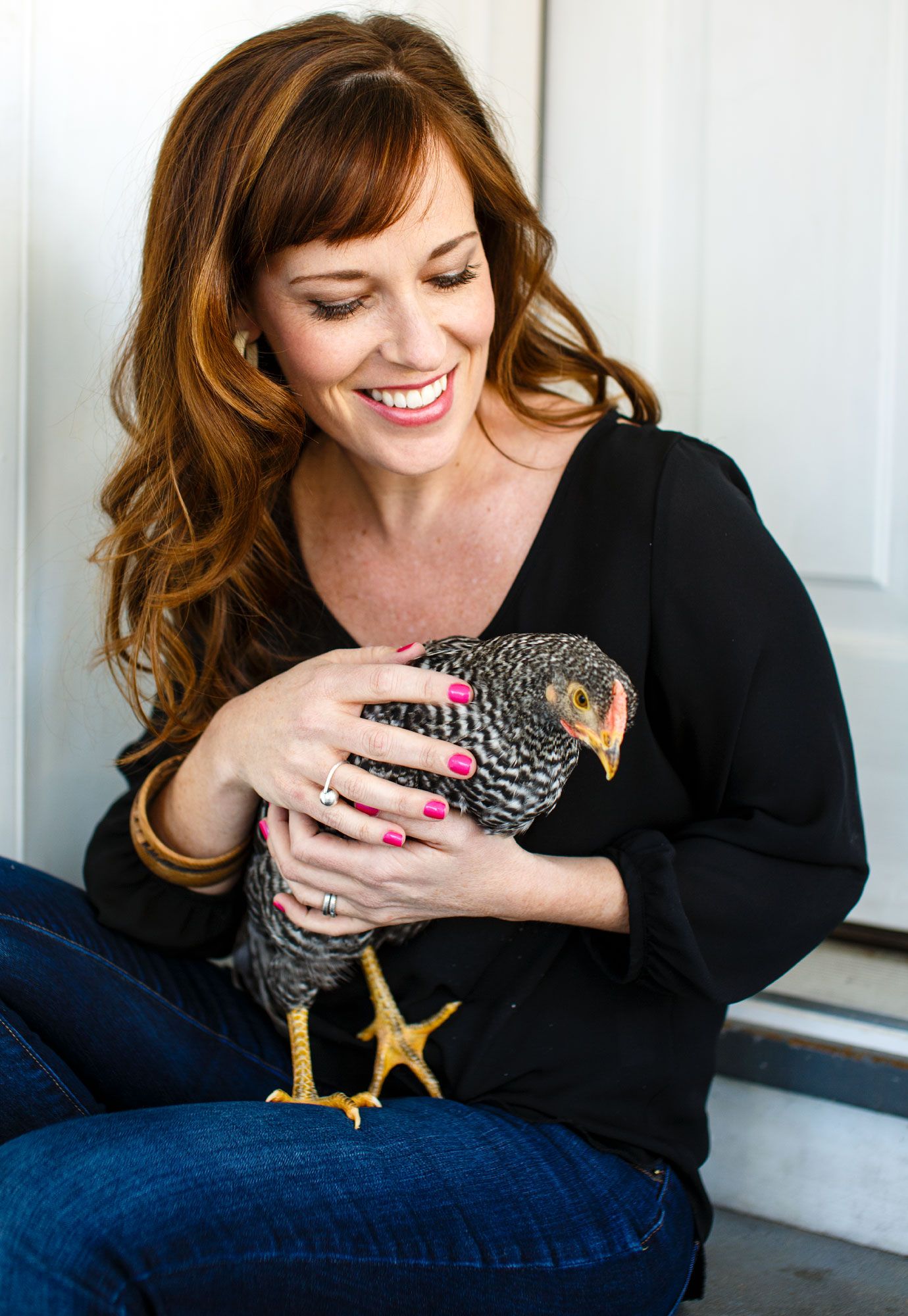 Smiling woman with red hair holding a young chicken outdoors.