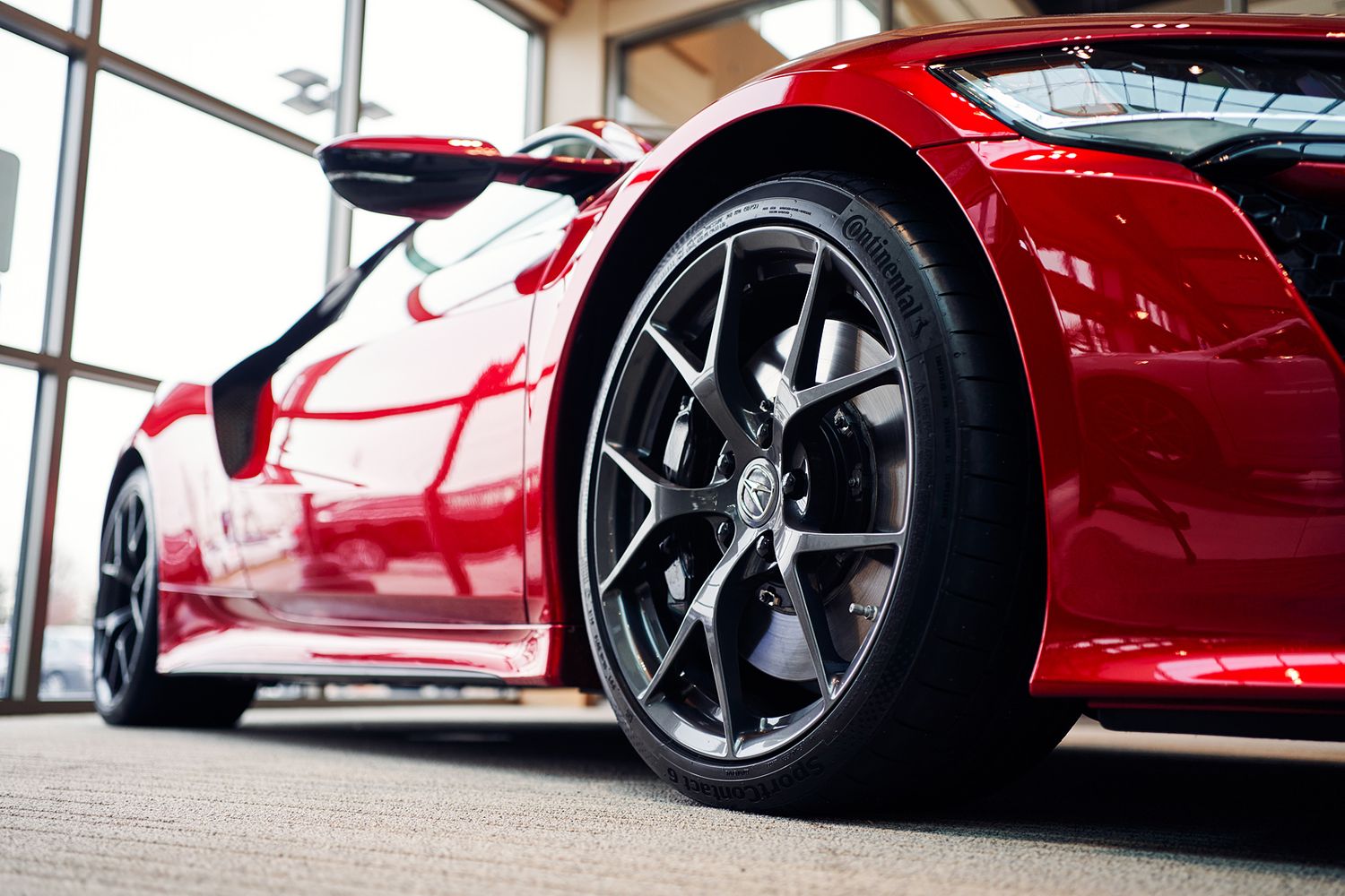 Close-up of a red sports car with black alloy wheels on a showroom floor.