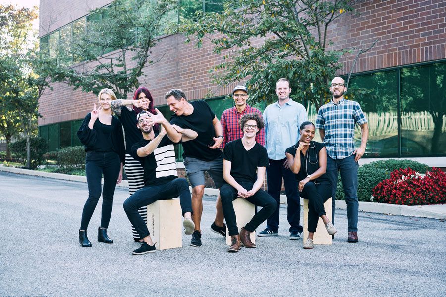 Diverse group of smiling coworkers posing together outdoors in a fun team photo outside an office building.