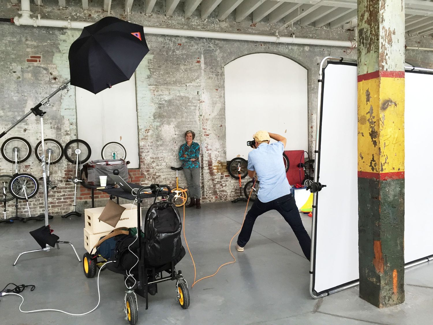 Photographer using umbrella flash lighting to photograph a subject in a rustic brick warehouse studio.