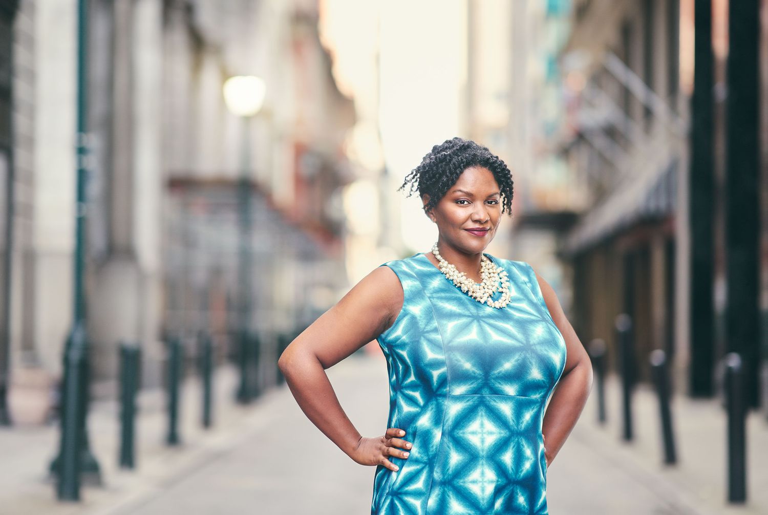 Woman in teal dress posing confidently on urban street.