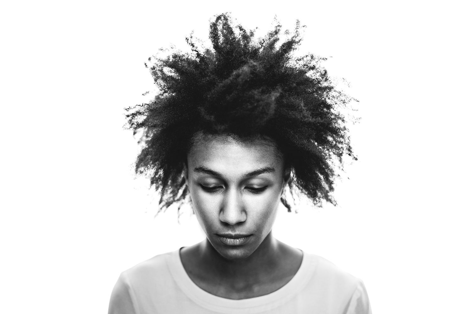 Black and white portrait of young woman with natural afro hairstyle looking downward.