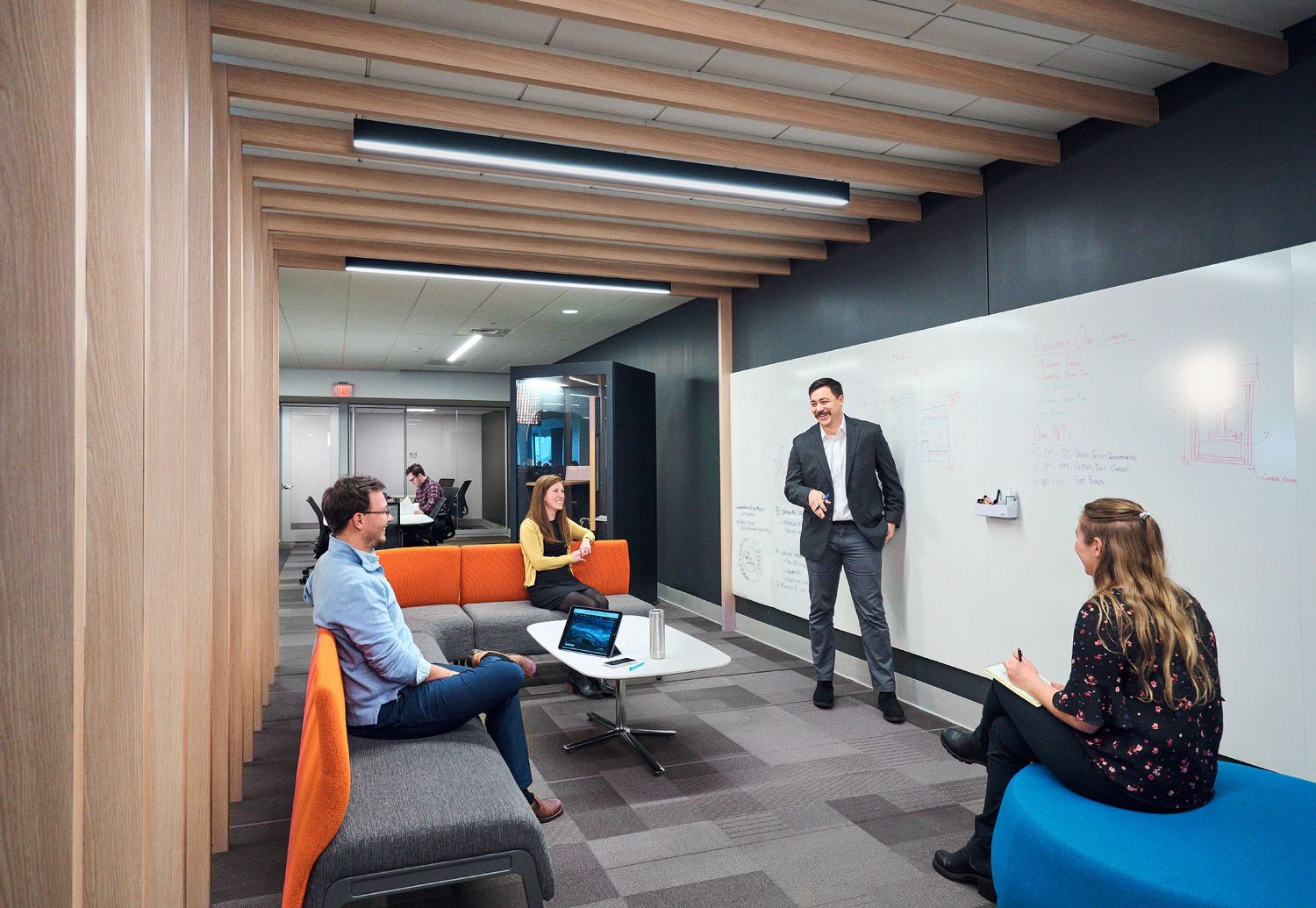 Small team collaborates in a modern open office space with a whiteboard and colorful seating.
