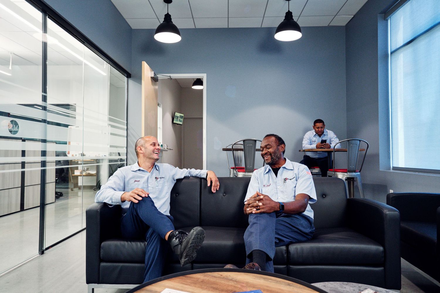 Two logistics employees relaxing and conversing on sofas in a modern office break area.