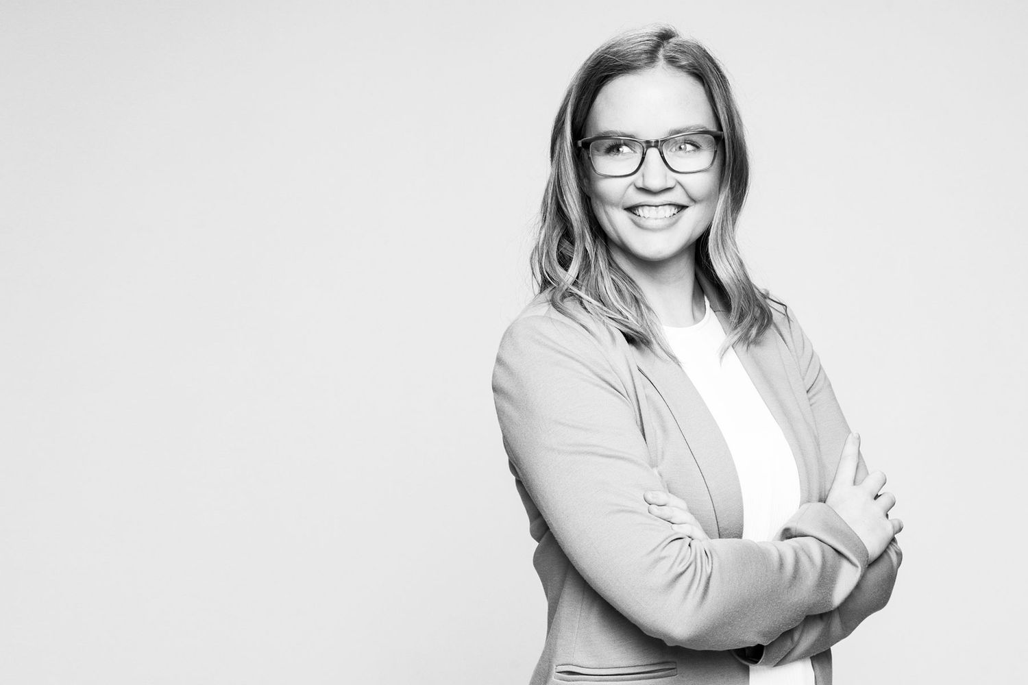 Black and white portrait of a smiling woman with glasses in a blazer with arms crossed.