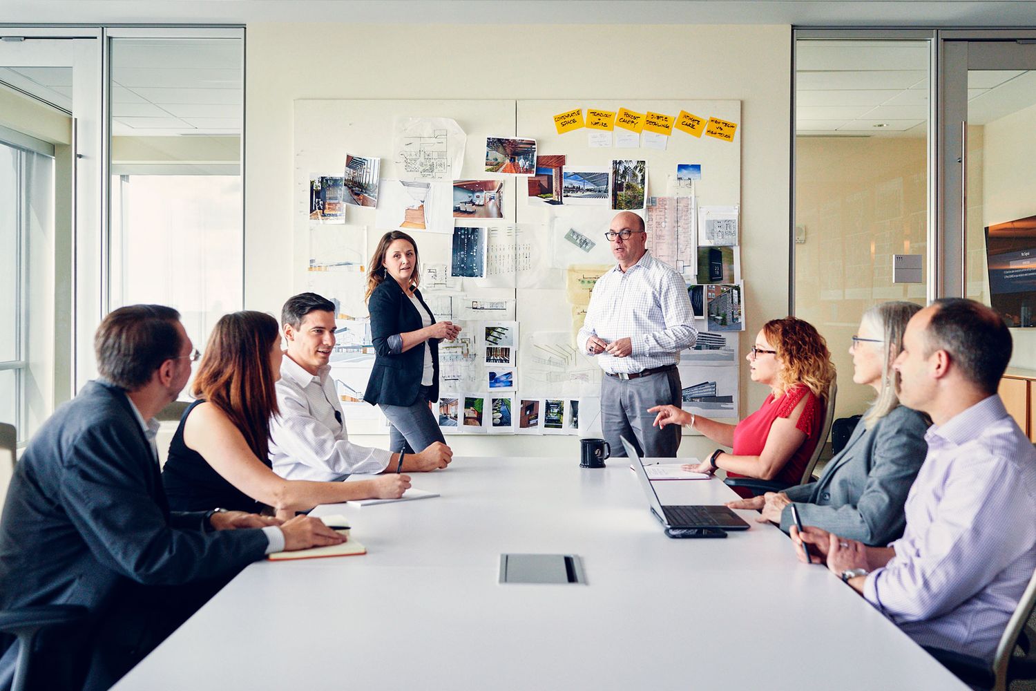 Team of seven professionals in a boardroom presentation with photos and charts on the wall.