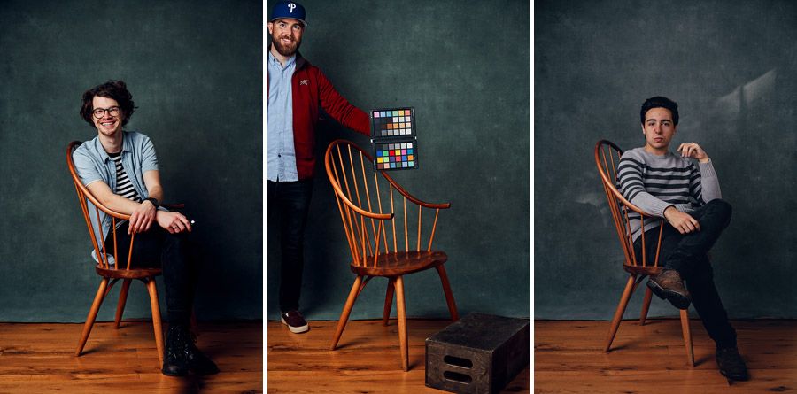 Three people posing with a wooden chair against a dark studio background.