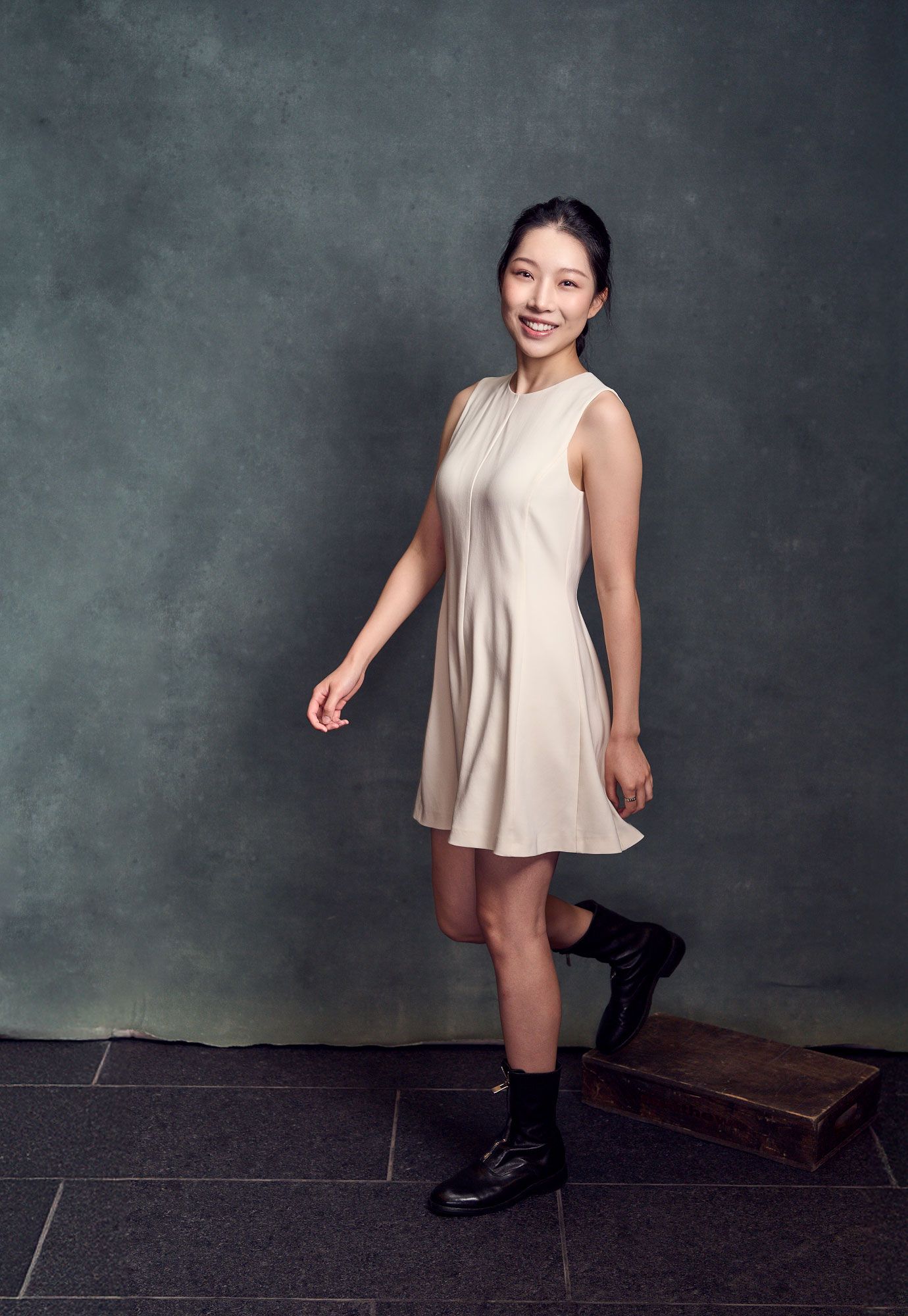 Young woman in cream dress posing in studio setting.
