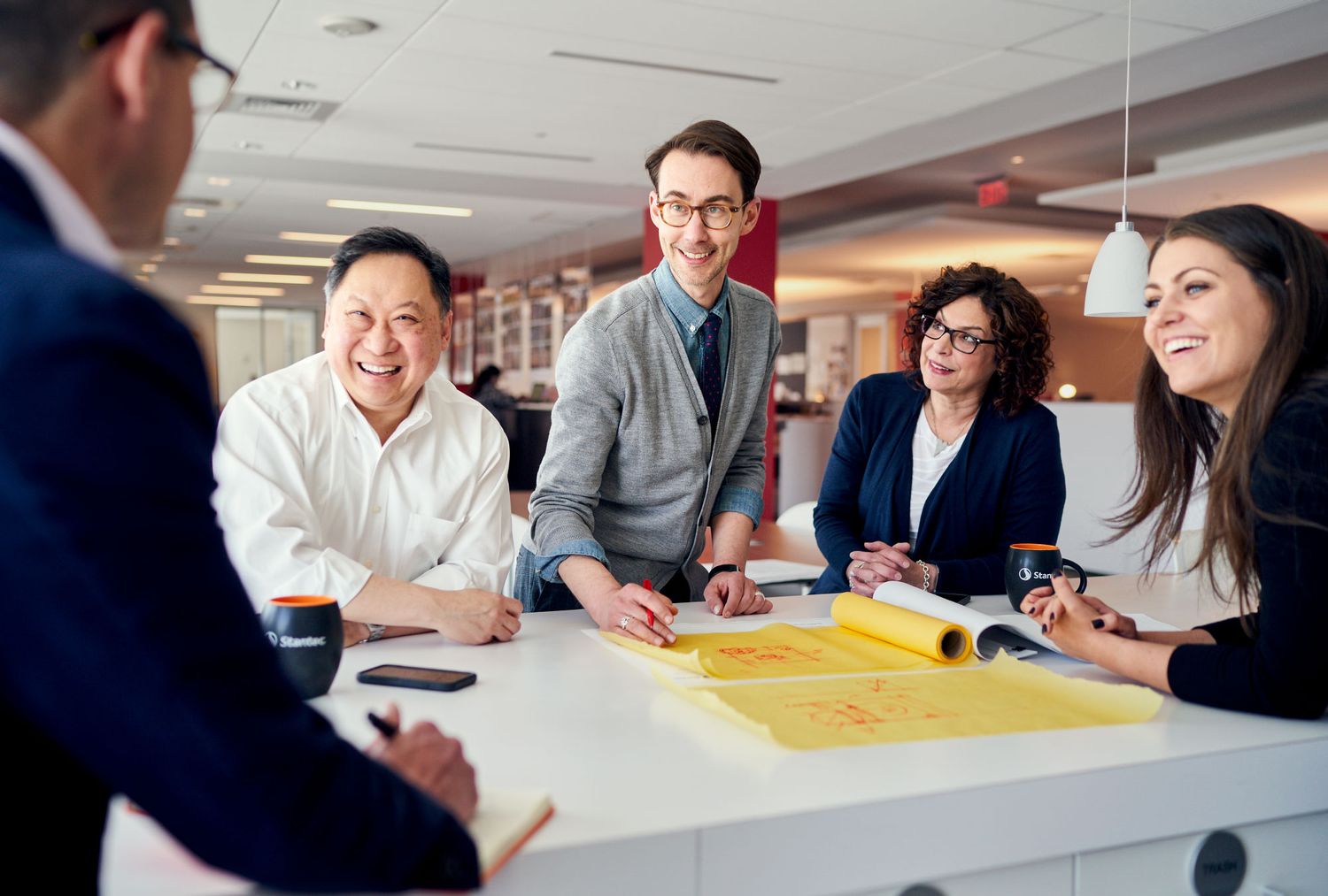 Diverse business team collaborating around a table with blueprints in a modern office.