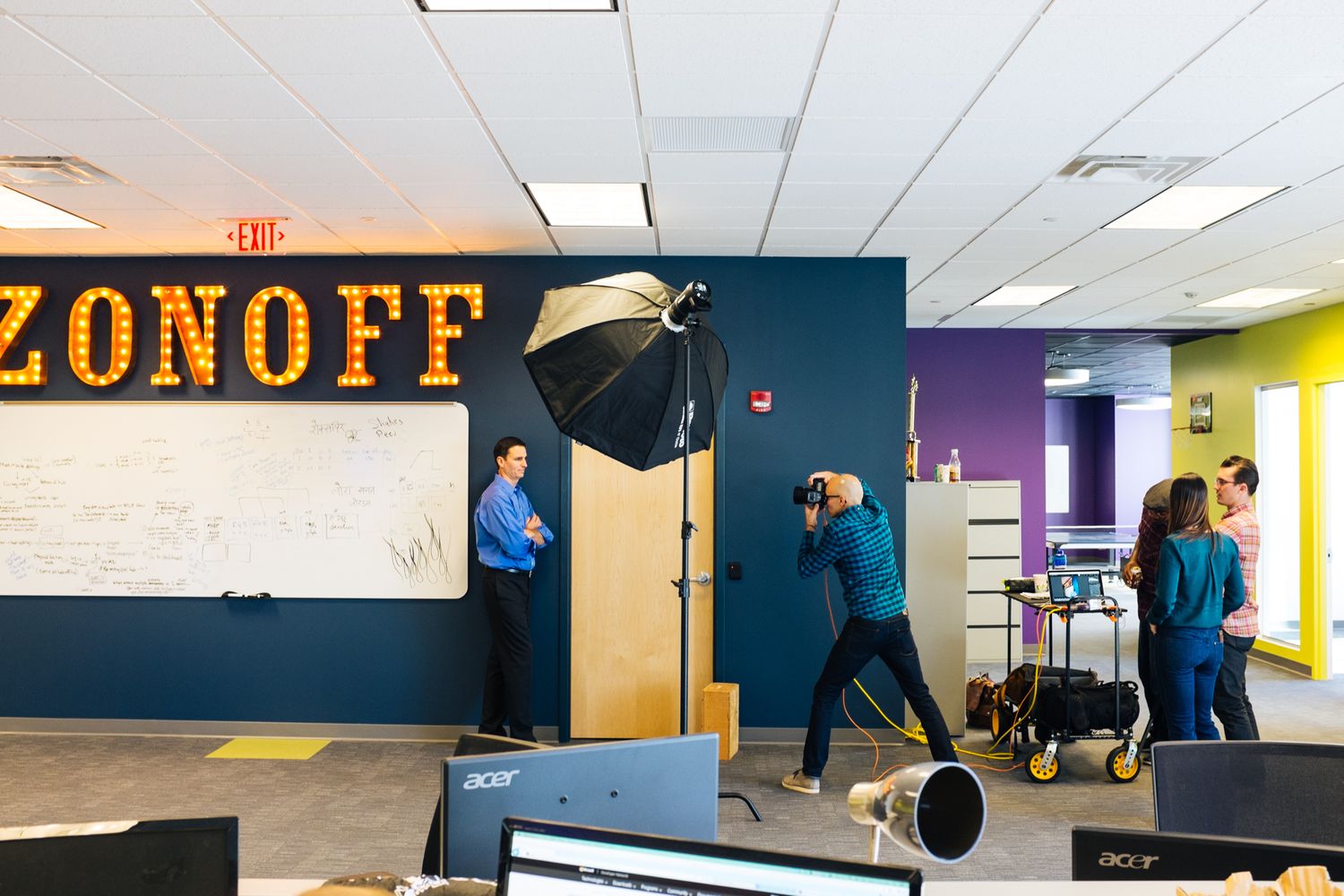 A photography crew shoots a professional photo in a colorful modern office with bright yellow and blue walls.
