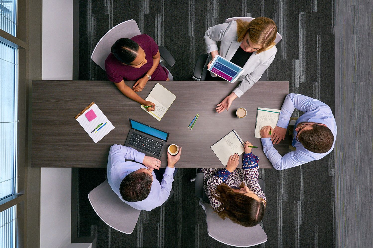 Overhead view of five professionals working together around a conference table with laptops.