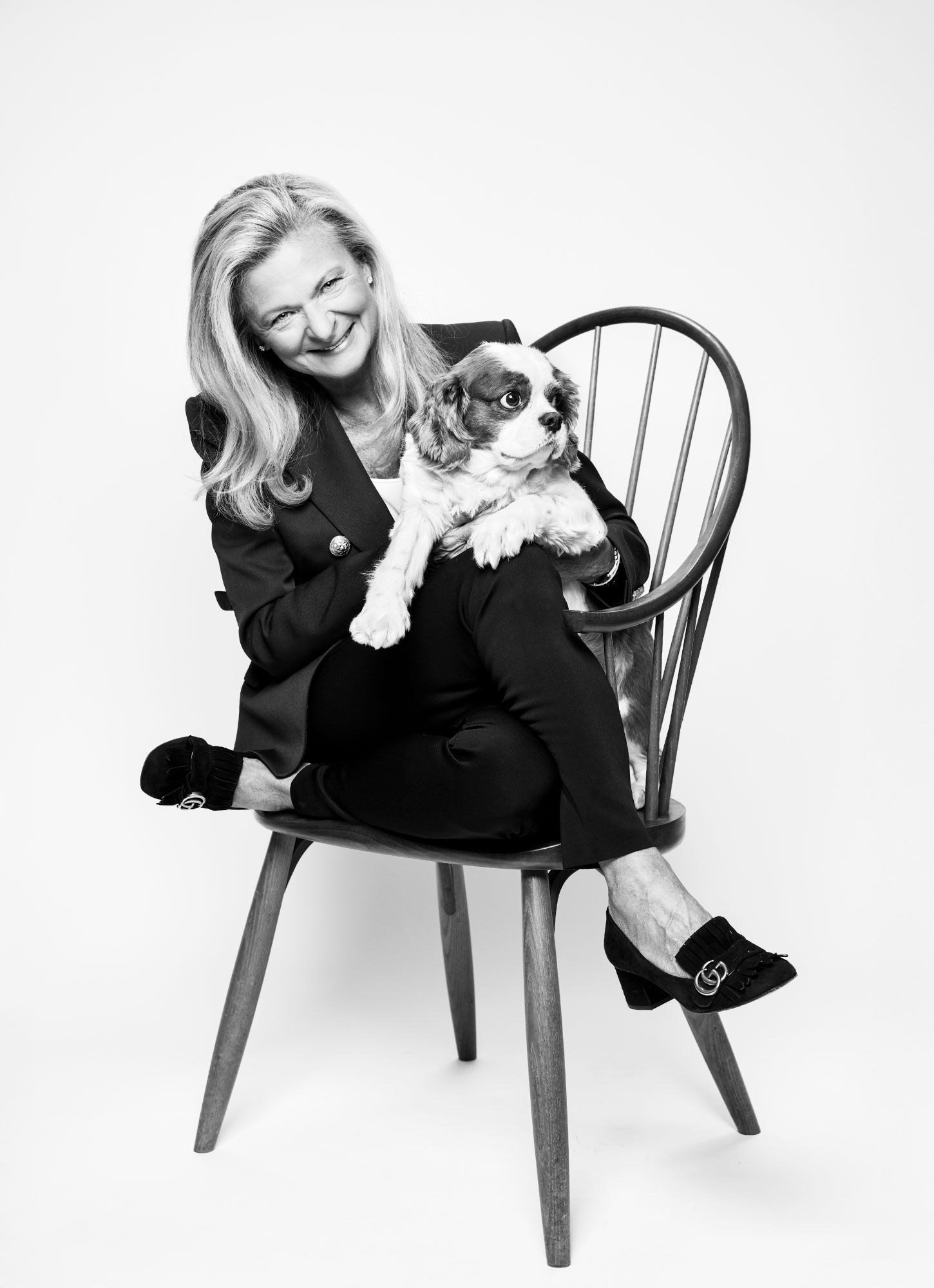 Black and white photo of smiling woman sitting in Windsor chair holding a small spaniel dog.