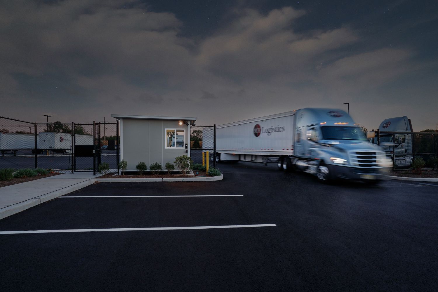 Semi-truck exiting a secured logistics facility gate at night.