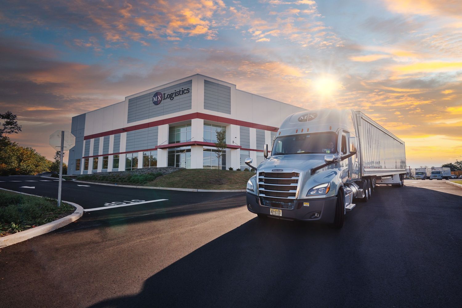 Semi-truck departing a large logistics warehouse facility at golden hour sunrise.
