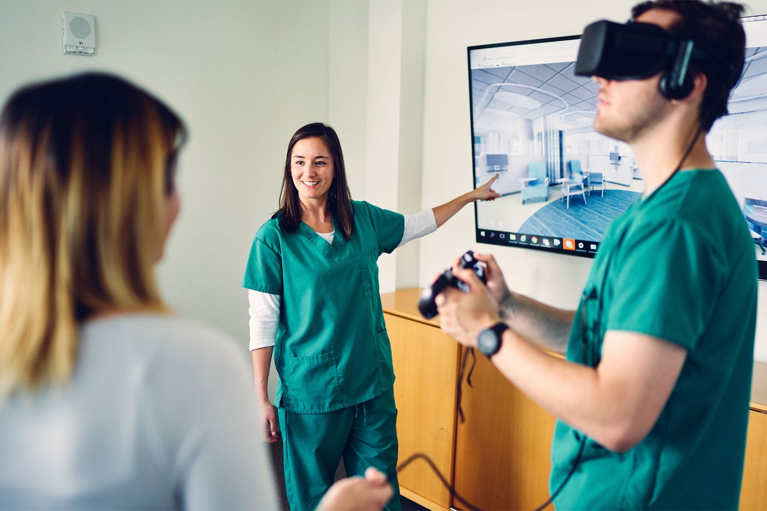 Healthcare workers in green scrubs using virtual reality technology to explore a medical environment.