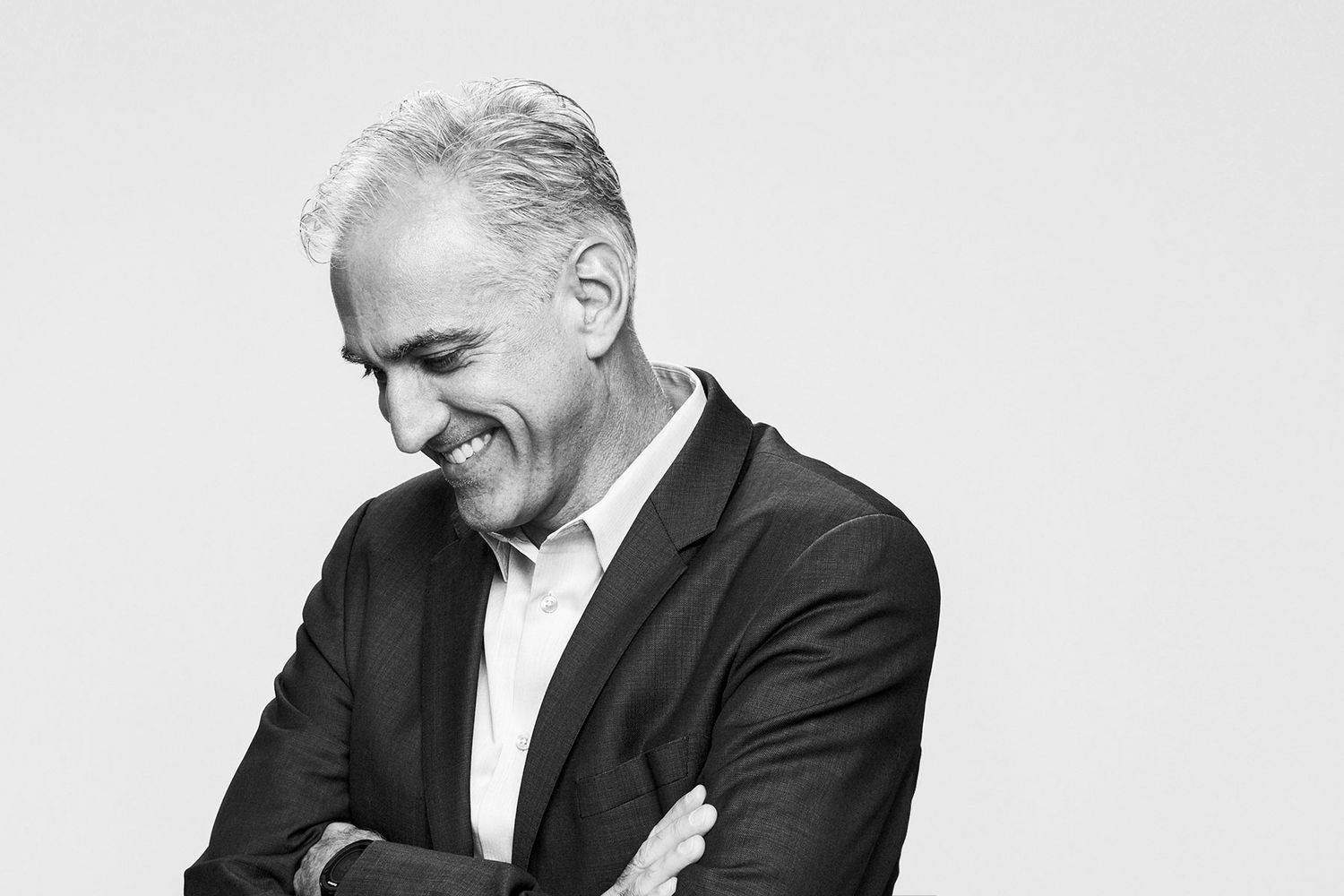 Black and white portrait of a silver-haired man in a suit smiling with arms crossed.