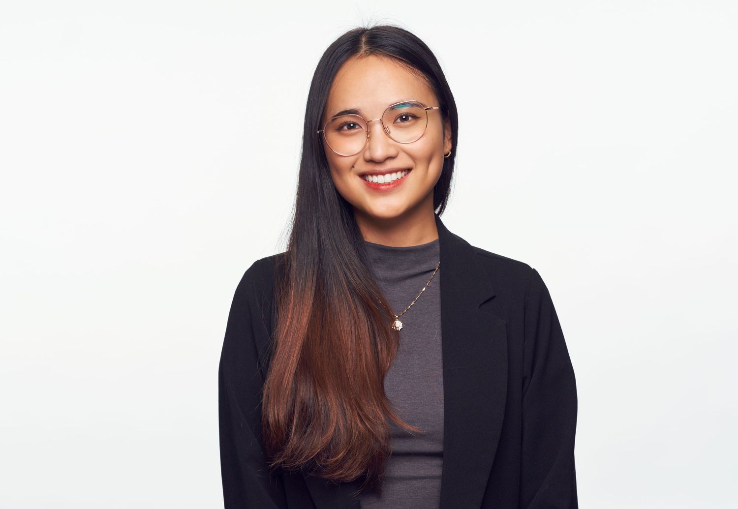 Young professional woman in black blazer smiles warmly against a clean white background.