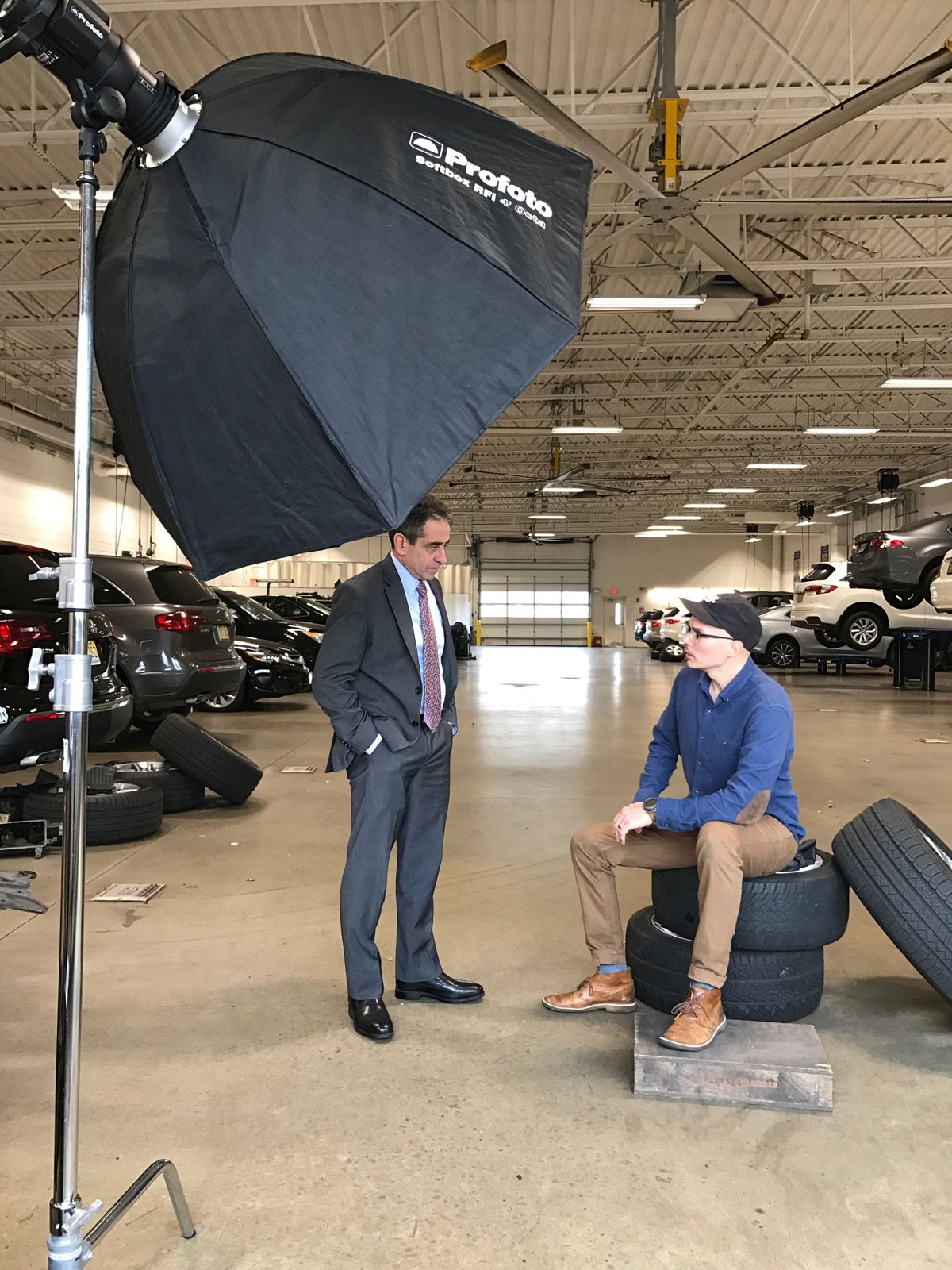 Two men in a car dealership garage during a professional photo shoot with a Profoto softbox light.