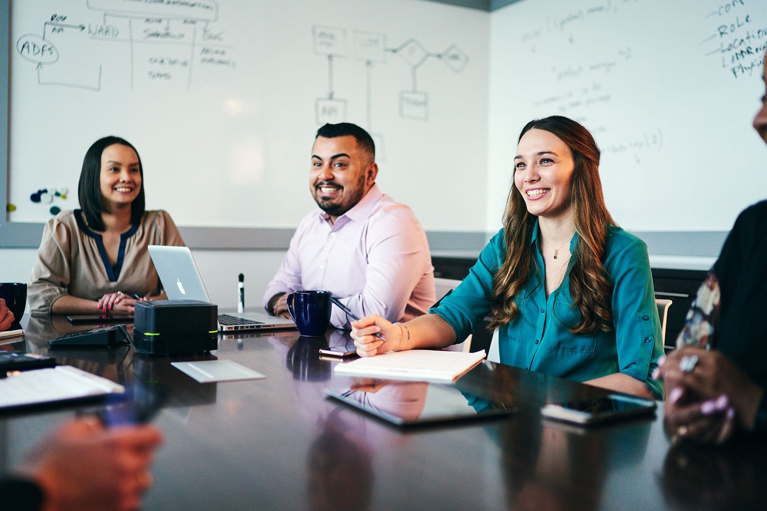 Diverse business team smiling during a meeting in a modern conference room with a whiteboard in the background.