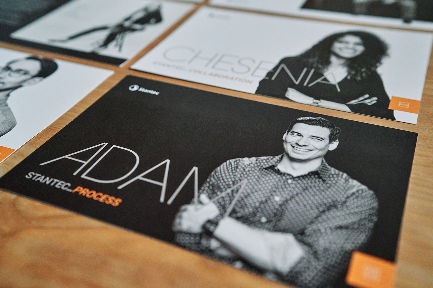 Black and white printed photo cards of professionals with orange Stantec branding on a table.