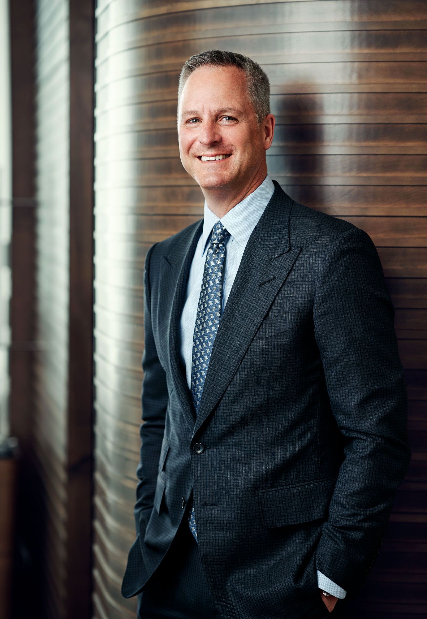 Confident businessman in dark suit and tie smiling with hands in pockets in elegant interior.