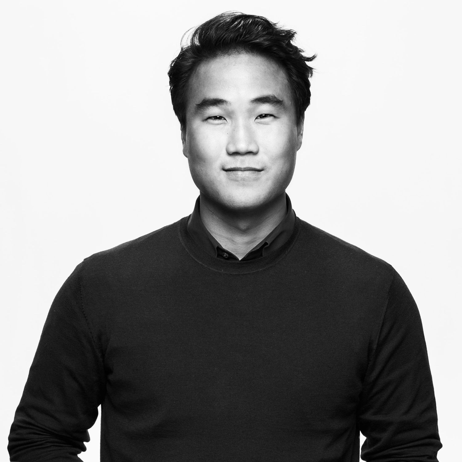 Black and white portrait of young man in black sweater against white background.