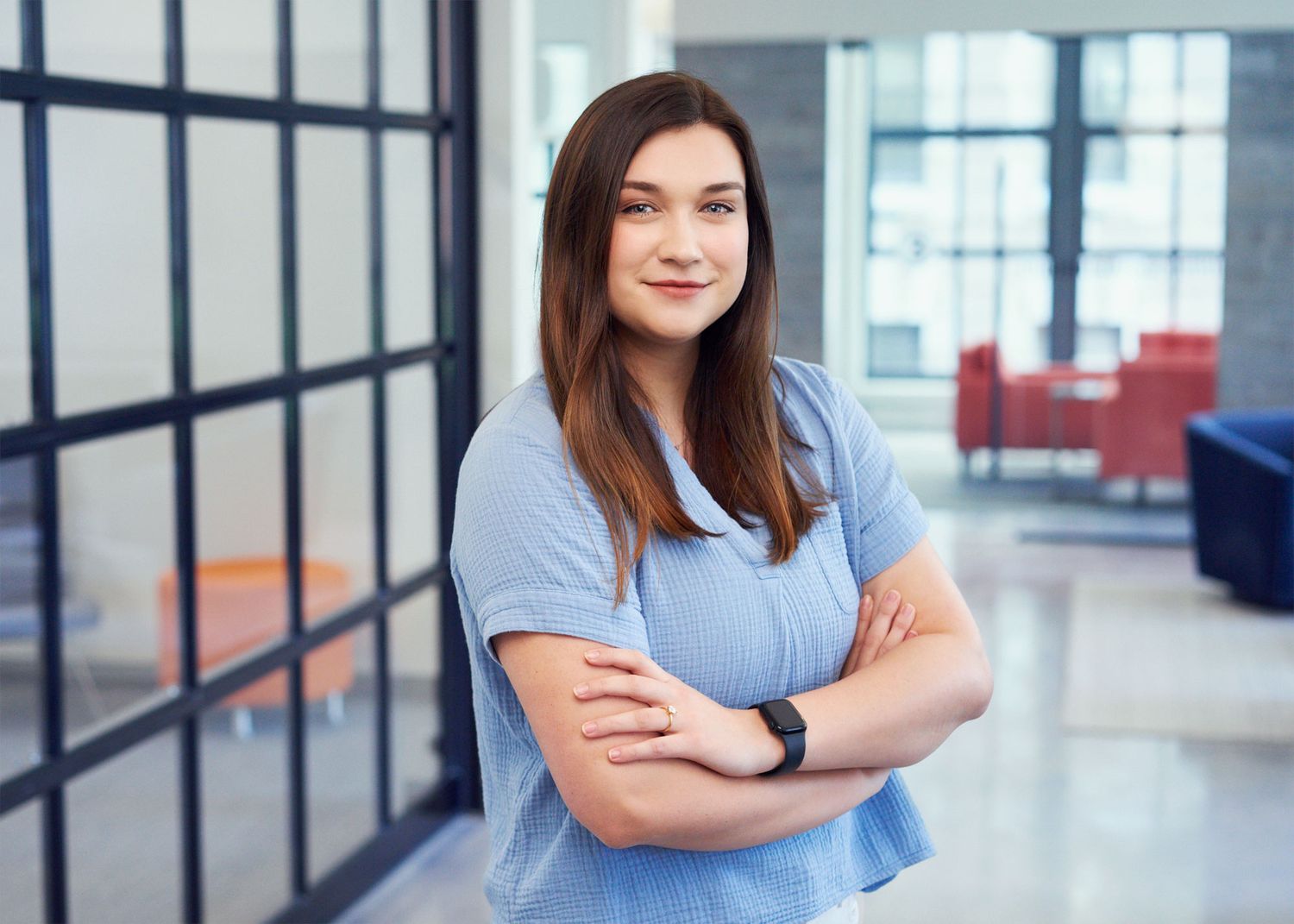 Young woman with brown hair standing arms crossed in modern office building.