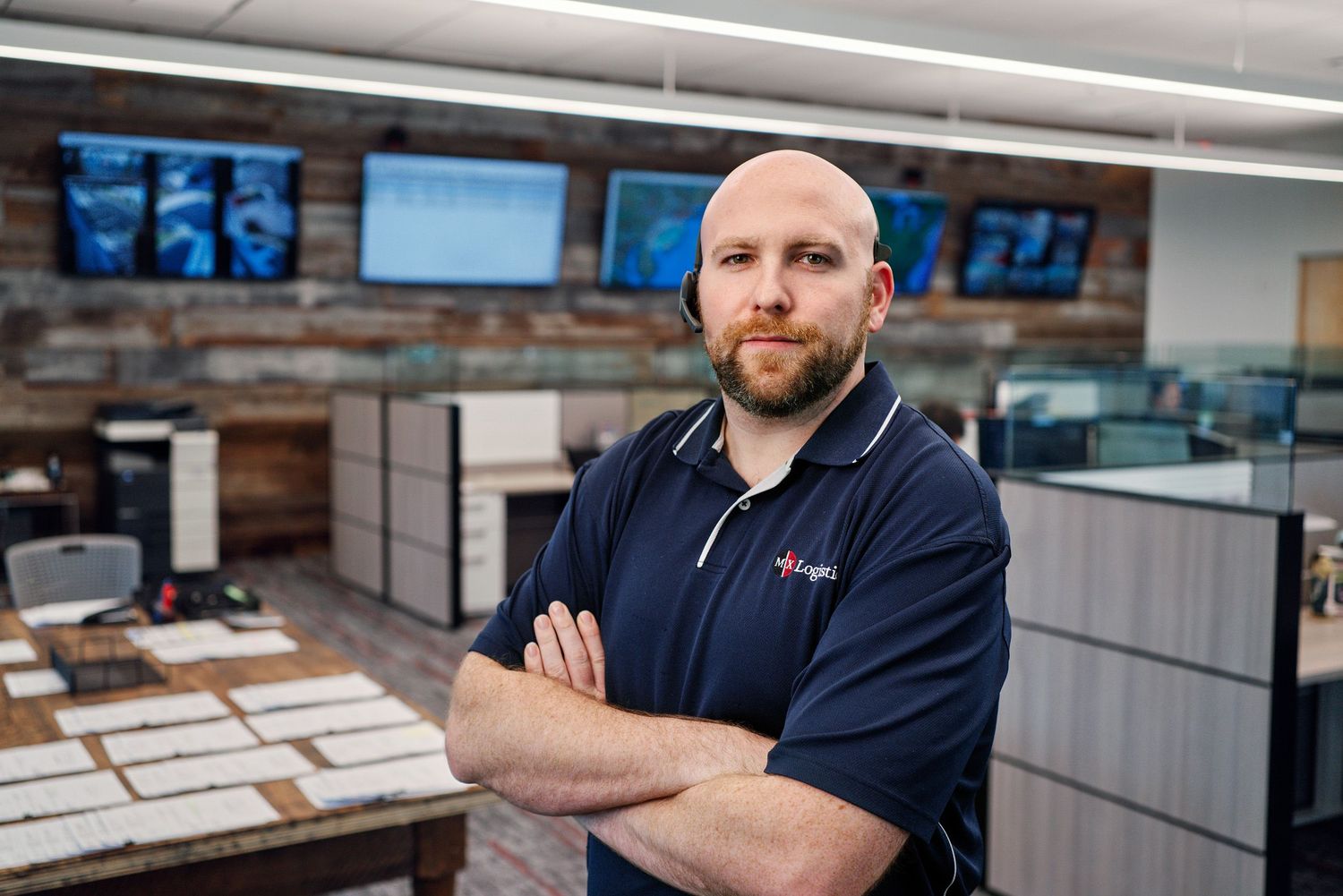 Confident logistics professional standing with arms crossed in a modern operations control center.