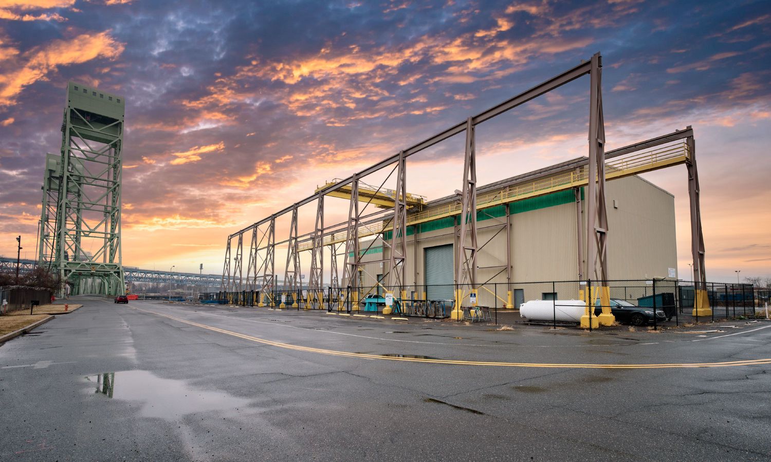 Industrial warehouse exterior with green steel framework at sunset with dramatic cloudy sky.