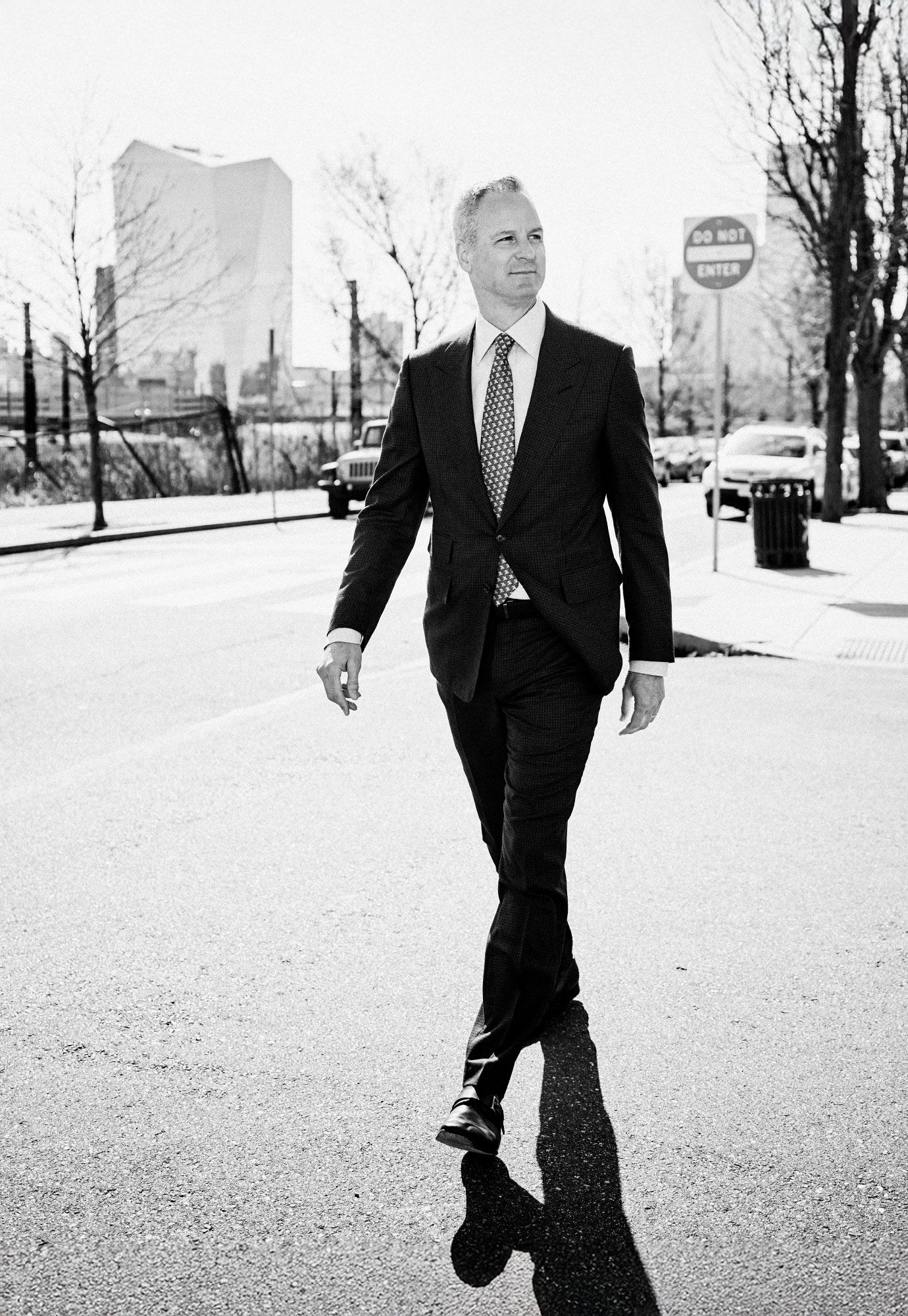 Black and white photo of businessman in dark suit walking confidently on urban street.
