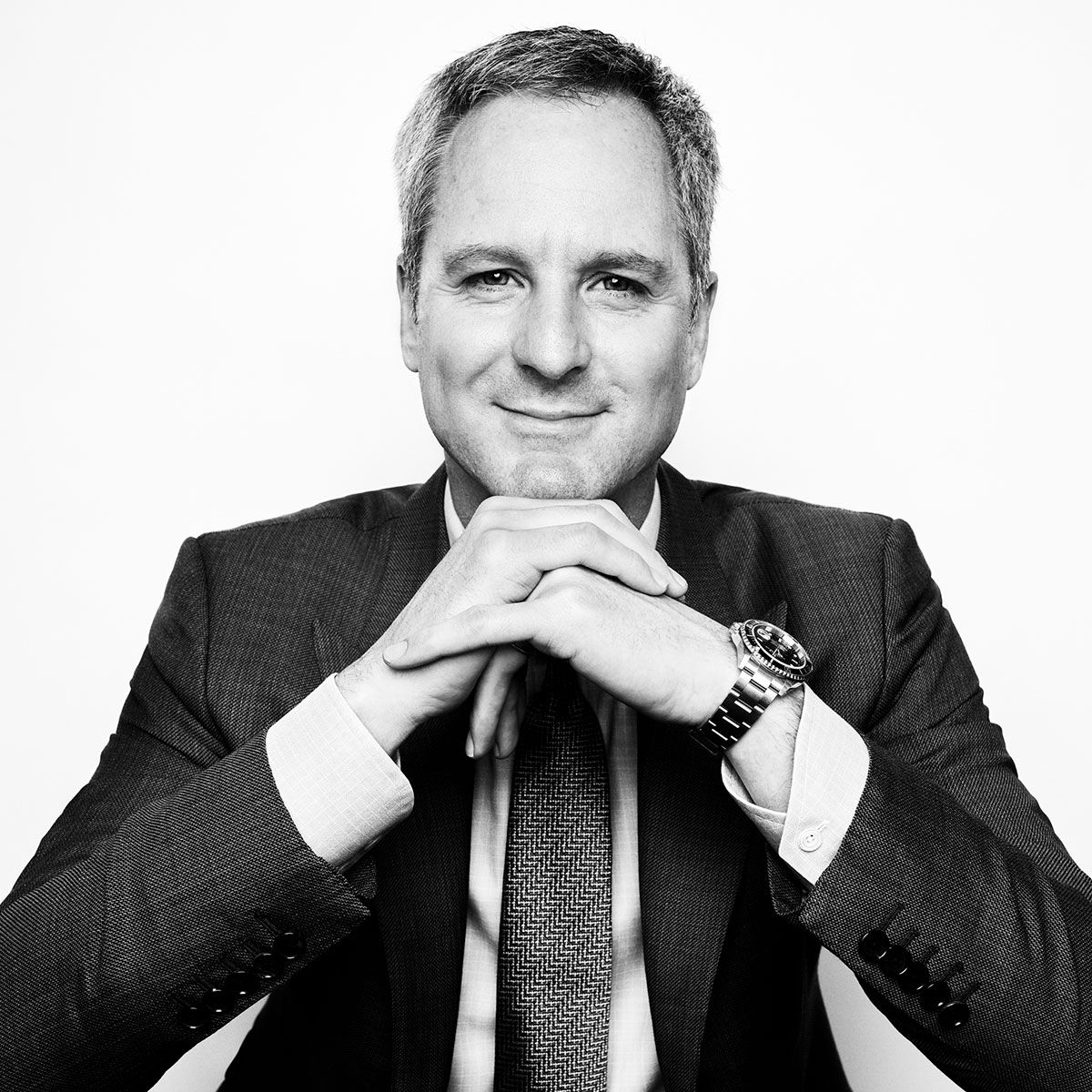 Professional businessman in suit with clasped hands, wearing a watch, black and white portrait photo.